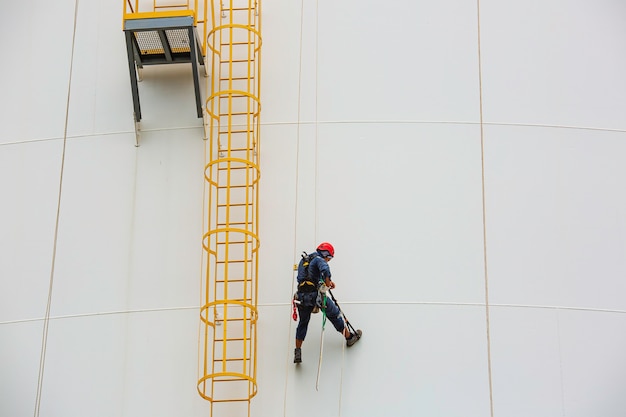 I lavoratori di sesso maschile controllano la fune verso il basso altezza del serbatoio accesso alla fune ispezione dello spessore della lamiera di rivestimento del serbatoio di stoccaggio del lavoro di sicurezza in altezza.