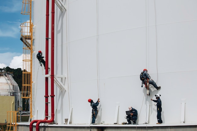 Male workers control under rope down height tank rope access
inspection of thickness shell plate storage tank safety work at
height.