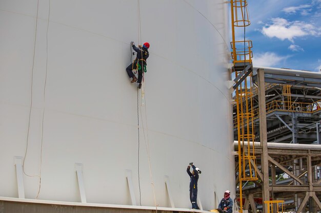 Male workers control rope down height tank rope access\
inspection of thickness shell plate storage tank.