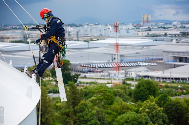 男性労働者は、高所での厚さシェルプレート貯蔵タンクガス安全作業のトップルーフタンクロープアクセス検査でロープを制御します。