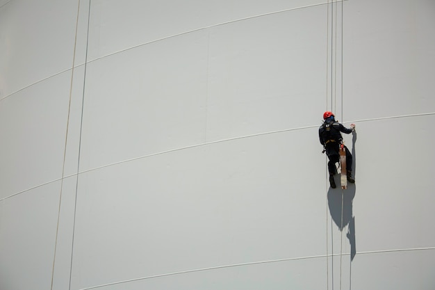 Male workers control swing rope down height white tank rope inspection of thickness tank gas.