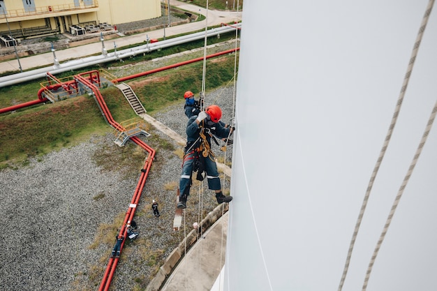 Male workers control swing rope down height white tank rope inspection of thickness tank gas.