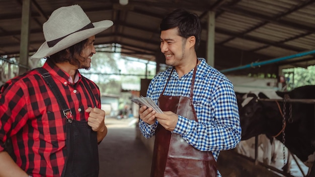 Male workers pay money and shake hands with farmers on the dairy farmAgriculture industry farming and animal husbandry concept Cow on dairy farm eating hay Cowshed small business