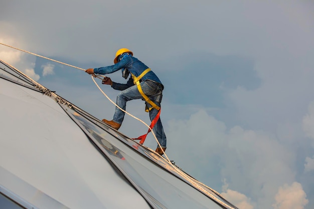 Male workers rope access height safety connecting with a knot safety harness clipping into roof construction site oil tank dome