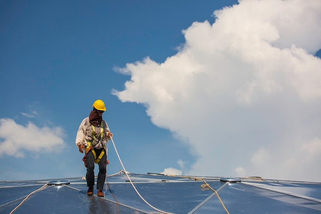 男性労働者は、結び目安全ハーネスで接続するロープアクセス高さの安全性、上昇する準備ができている屋根の落下阻止および落下抑制アンカーポイントシステムへのクリップ、建設現場の石油タンクドーム