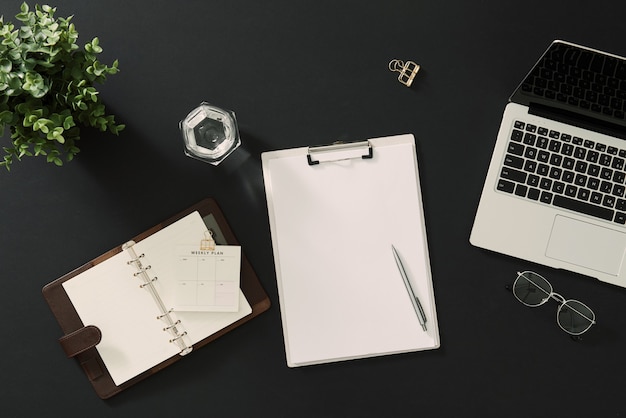 Male workspace with paper notebook, pen, accessories on dark .