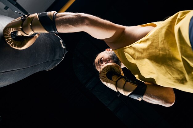 male in yellow sleeveless shirt placing a punch to a boxing bag