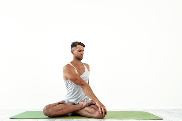 Male yoga maditates in classical pose in studio on white 