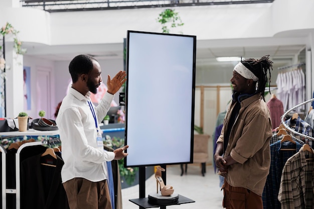 Mall-medewerker adverteert schoenenmerk voor koper, met gloednieuwe collectie op lege digitale whiteboard-mock-up. Winkelassistent die stiletto aan de klant laat zien op een interactief display