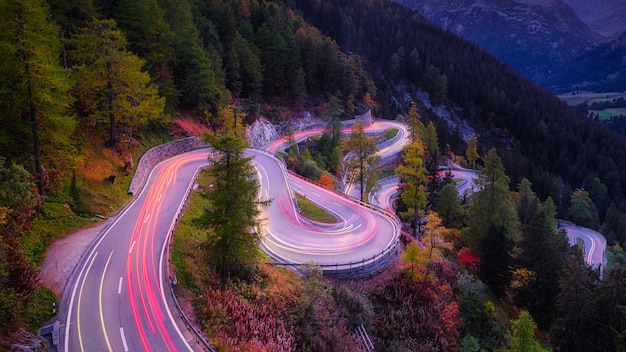 Maloja pass Switzerland A road with many curves among the forest A blur of car lights Landscape in evening time