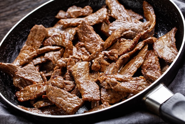 Mals en sappig gebakken ribeye biefstuk in reepjes gesneden, minuut steak, op een koekenpan op een donkere houten tafel, horizontale weergave van bovenaf