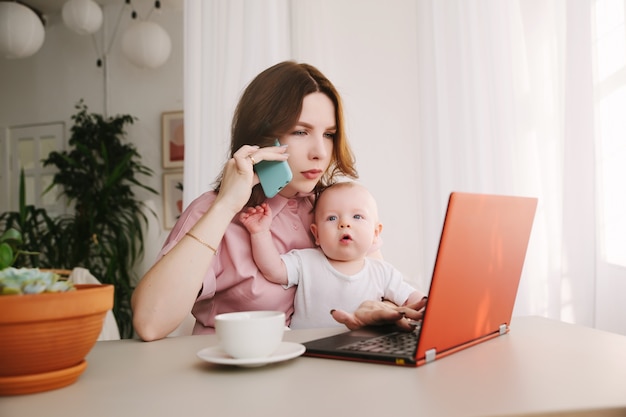 Mam en baby. een jonge moeder die werkt met laptop in en praten over de telefoon.