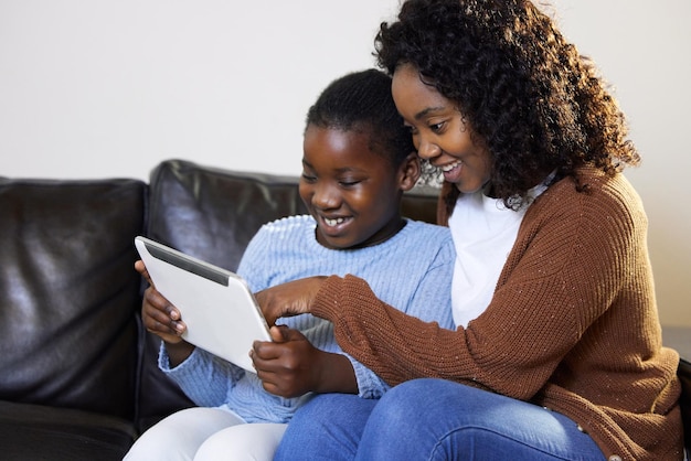 Mam kijk wat ik deed Shot van een aantrekkelijke jonge moeder die met haar dochter in de woonkamer zit en een digitale tablet gebruikt