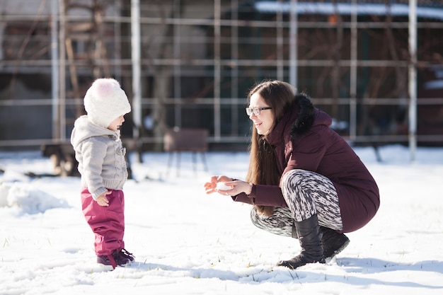 Mam laat de sneeuw aan een klein meisje zien op de koude, zonnige winterdag