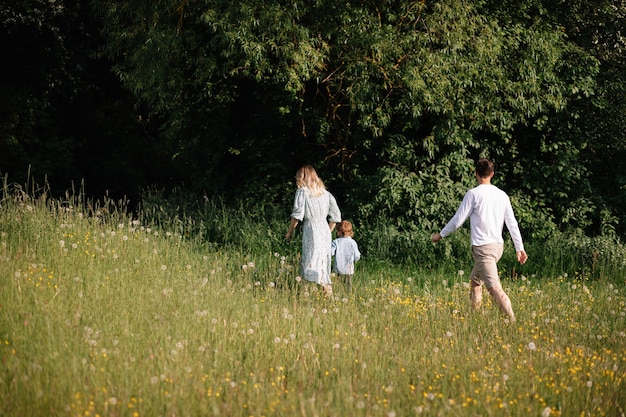 mama en papa maken een wandeling langs bos en veld met bloeiende weiden met hun 3-jarige zoon