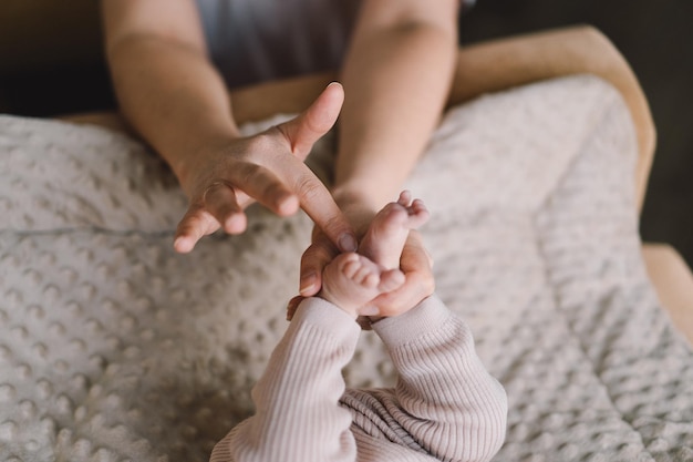 Mama maakt babymassage moeder masseert zuigeling blote voet preventieve massage voor pasgeboren mama streelt de voeten van de baby met beide handen Liefde baby Pasgeboren baby en moeder