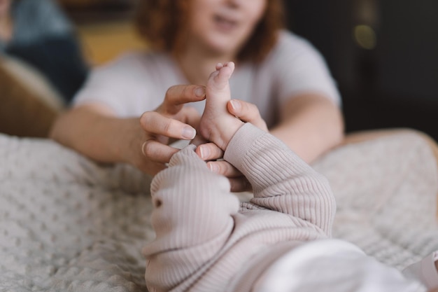 Mama maakt babymassage moeder masseert zuigeling blote voet preventieve massage voor pasgeboren mama streelt de voeten van de baby met beide handen Liefde baby Pasgeboren baby en moeder