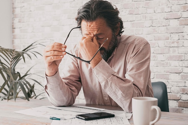 Man aan de balie ontvangt slecht nieuws aan de telefoon en raakt zijn voorkant met wanhoop zakelijke problemen mensen in het kantoor Een volwassen professionele freelancer met migraine en vermoeid gestrest