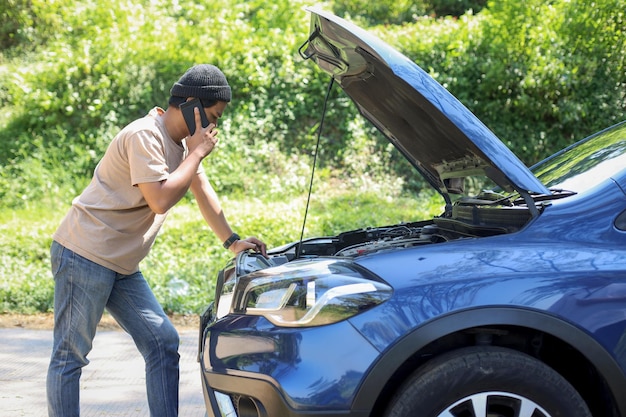 man aan de telefoon om een monteur te vragen om zijn kapotte auto op de snelweg te komen repareren