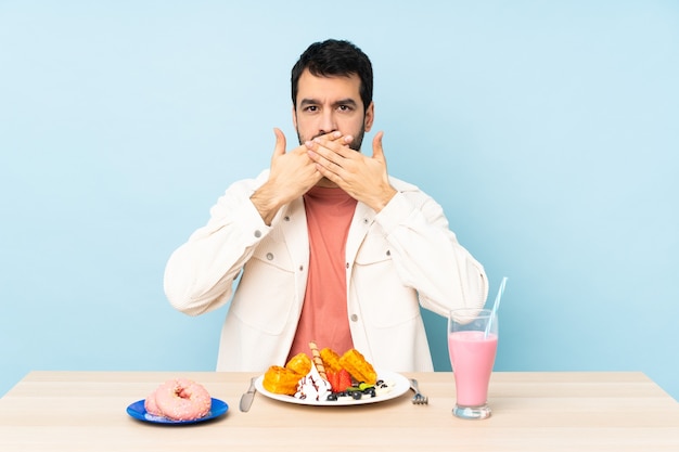 Man aan een tafel met ontbijtwafels en een milkshake die mond bedekt met handen