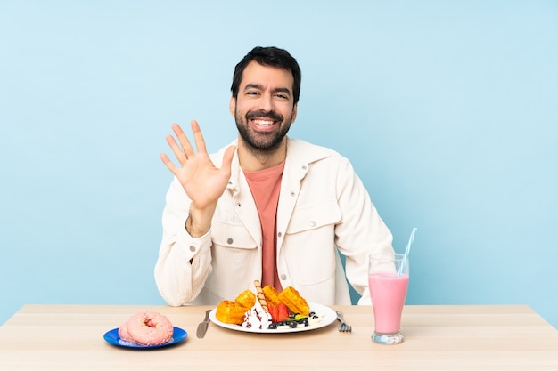 Man aan een tafel met ontbijtwafels en een milkshake die vijf telt met vingers