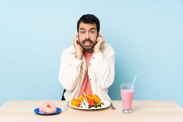 Man aan een tafel met ontbijtwafels en een milkshake gefrustreerd en oren bedekkend