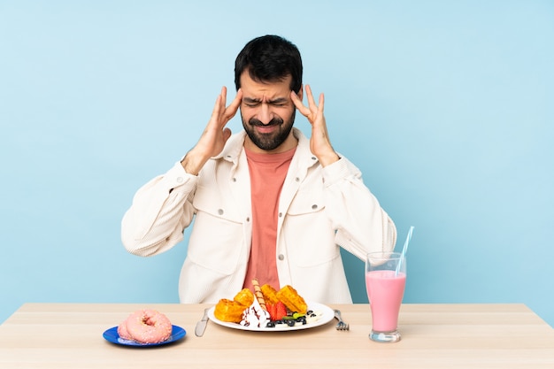 Man aan een tafel met ontbijtwafels en een milkshake met hoofdpijn