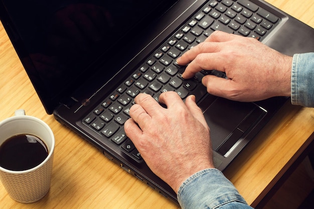 Man aan het werk met zijn laptop op een houten tafel