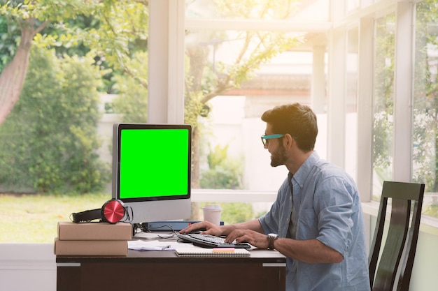 Foto man aan het werk op het groene computerscherm in zijn thuiskantoor 's avonds wanneer de zon door de kamer schijnt