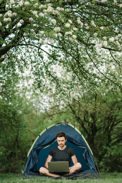 Man aan het werk op laptop in tent in de natuur