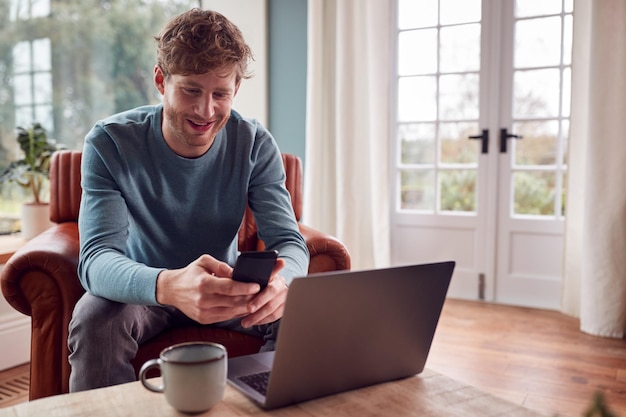 Man aan het werk vanuit huis met behulp van laptop en mobiele telefoon