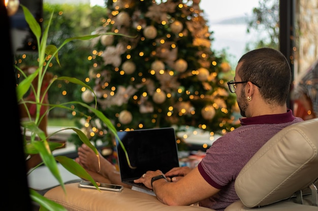 Man aan het werk vanuit huis op kerstachtergrond met wazige kerstboom