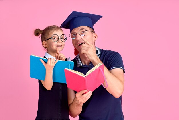 Man in academic hat holding book, study together with cute preteen girl in school uniform