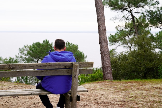 Man achteraanzicht terug zittend op een houten bankje kijken naar strand water meer in eenzaamheid