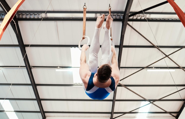 Foto uomo acrobata e ginnastica appesi agli anelli in forma fisica per l'allenamento pratico o l'allenamento in palestra ginnasta maschio professionista su cerchi ad anello sottostanti per acrobazie atletiche o esercizi di forza