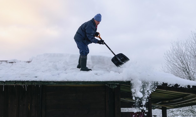 Man in action on the private house roof with shovel cleaning snow Danger job