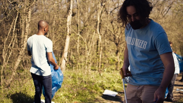 Photo man activist using tongs to grab garbage and plastic waste