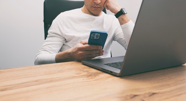 Photo man addicted to his phone surfing the social media on his phone while must works with his laptop