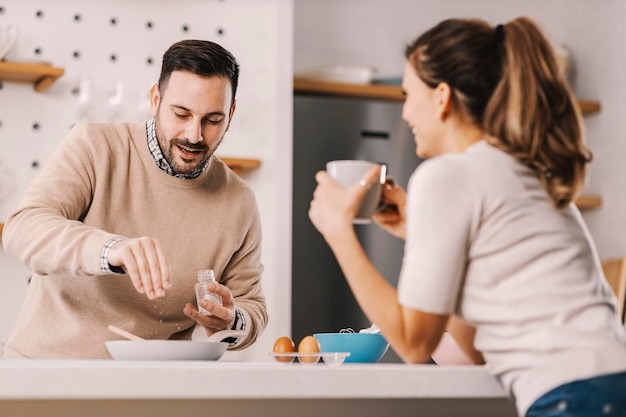 A man adding salt in breakfast while standing in kitchen with girlfriend