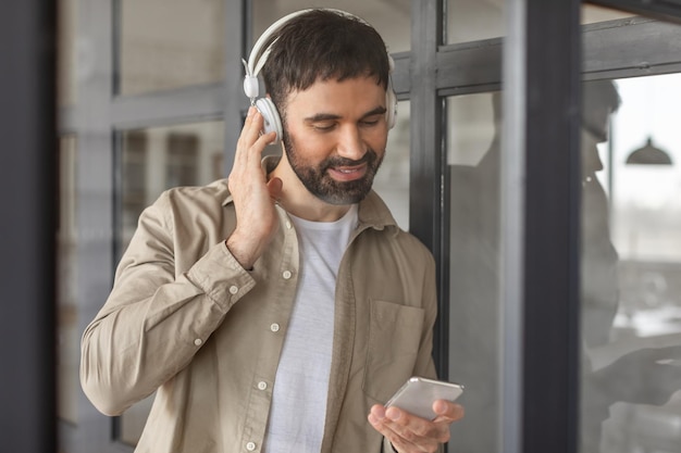 Man Adjusting Headphones While Holding Smartphone in Office Building