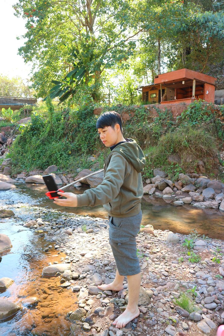 Photo man adjusting mobile phone in monopod against trees