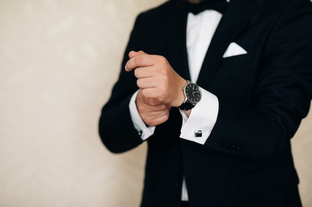 Man adjusting wristwatch in black tuxedo