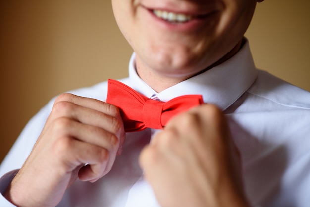 The man adjusts his red tie bow tie.