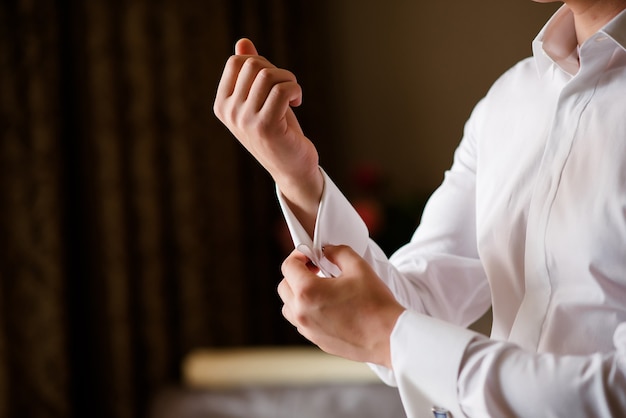 The man adjusts his sleeve on the white shirt.