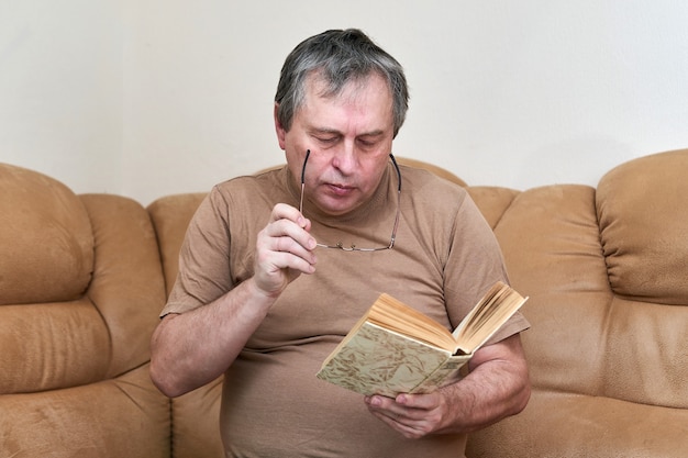 A man of age sitting on the devani is reading a book