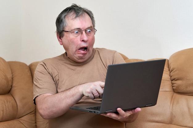 A man at the age of sitting on devani looks through the news on a laptop