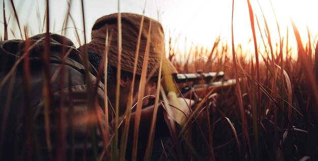 Man aiming rifle while lying on grassy field