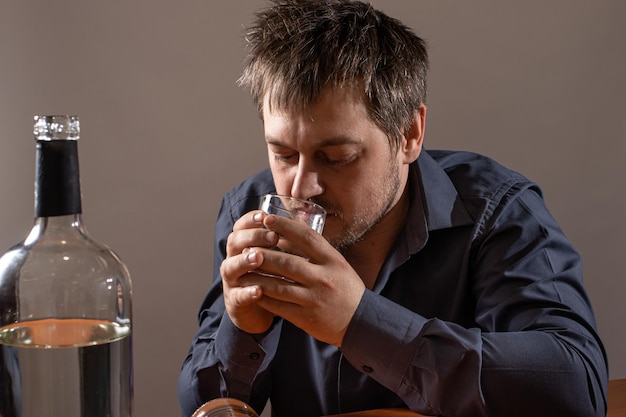 アルコール中毒の男性がコップ一杯のアルコールを持っています