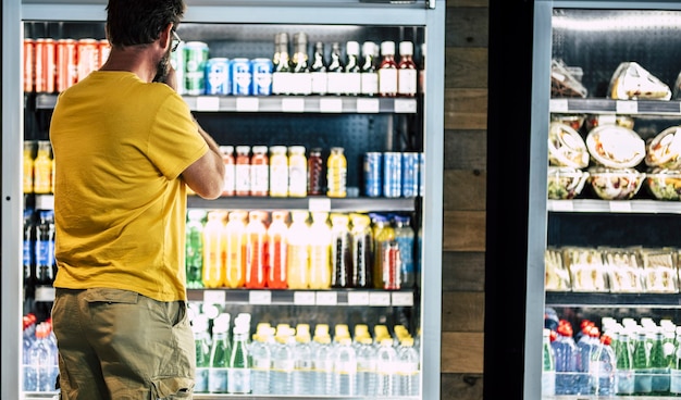 man alleen en geïsoleerd in de supermarkt of minimarkt die zijn drankje of snack kiest in een grote koelkast met veel producten