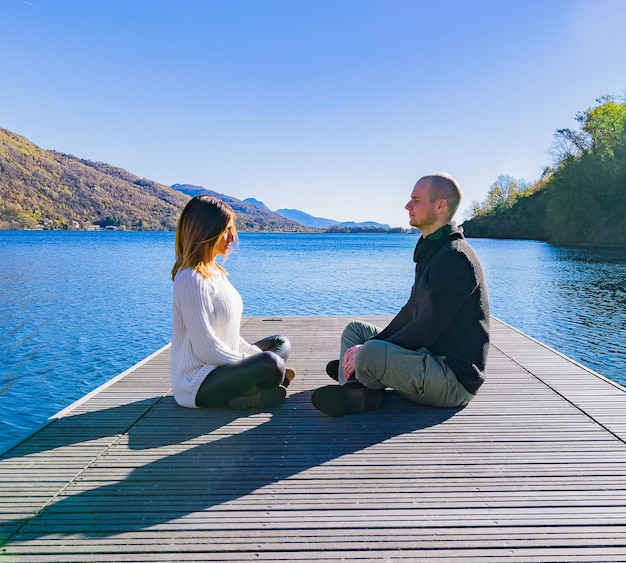 写真 明るい空の前で湖の埠頭に座っている男と女